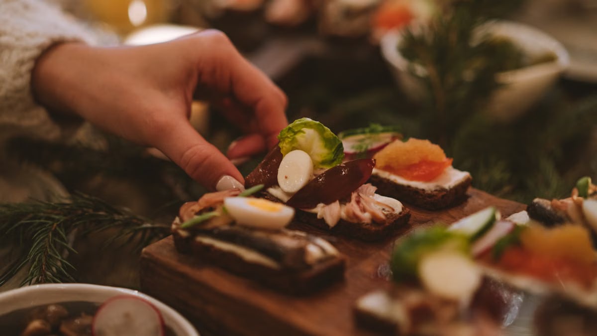 A hand reaches for a festive appetizer on a wooden board, surrounded by holiday decor.