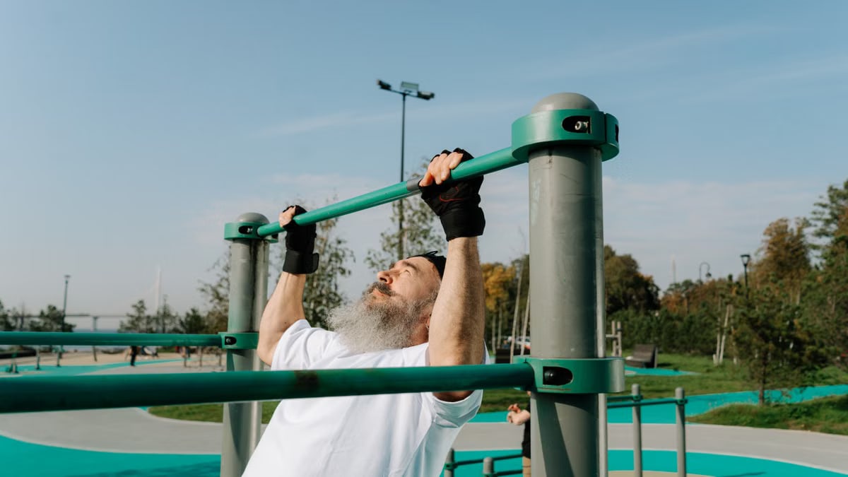 Senior man staying fit with pull-ups in an outdoor park setting, promoting healthy lifestyle.
